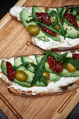 bruschetta with avocado, olives, arugula on a cutting board