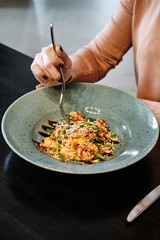Woman tastes pasta with seasame and herbs on dark background