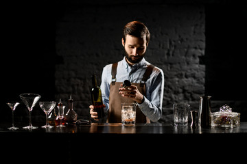 Professional male bartender with a beard pouring a alcoholic drink from the bottle to a steel jigger