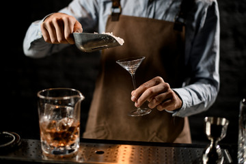 Professional bartender putting a crushed ice to the little martini glass with special spoon