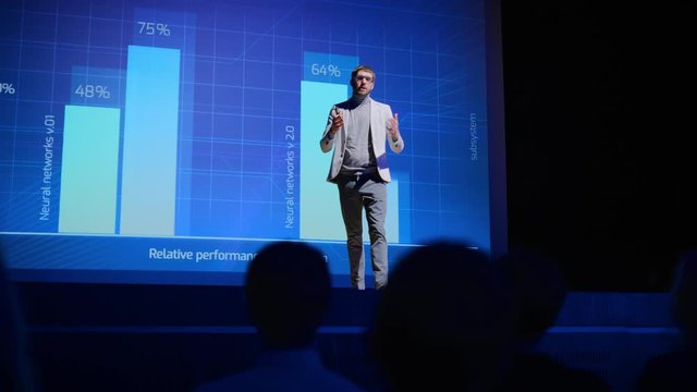 On-Stage Speaker Greets Audience, Presents Technology Product, Uses Remote Control for Presentation, Showing Infographics, Statistics Animation on Big Screen. Live Event / Start-up Conference