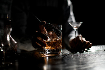 Professional bartender holding a measuring glass cup with a stainer half full of an alcoholic drink