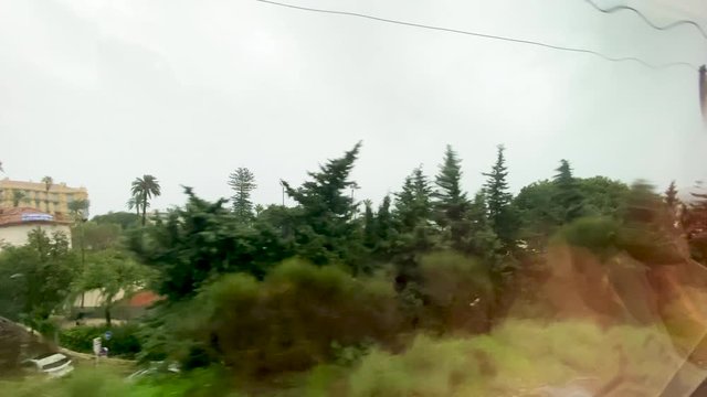 Cinematic 4k UHD Elevated view from the train rainy window over the NIce city periphery with small villas and tall palm trees - leaving departure arrival - rainy weather