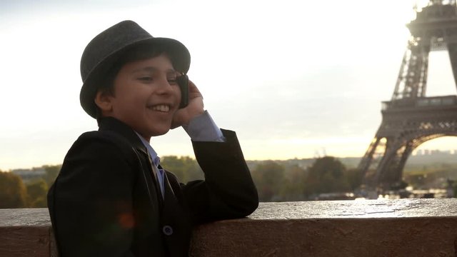 Beautiful teenager boy in a hat is speaking and laughing on the phone on the background of the Eiffel tower, Paris, France
