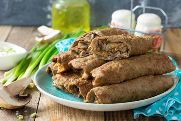 The concept of a healthy breakfast or snack. Meat liver pancakes stuffed with mushrooms and vegetables in a plate on rustic wooden table.