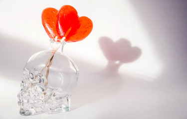 two heart-shaped candies stand in a skull-shaped jug on a white background