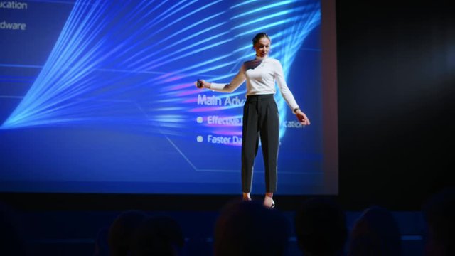 Female Speaker Gets on Stage, Greets Audience and Does Presentation Technological Product, Shows Infographics, Statistics Animation on Screen. Live Event / Device Release / Start-up Conference