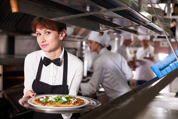 Smiling waitress with pizza in restaurant kitchen