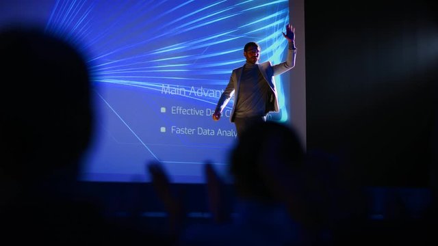 Male Speaker Gets on Stage, Greets Audience and Does Presentation of the Technological Product, Shows Infographics, Statistics Animation on Screen. Live Event / Device Release / Start-up Conference