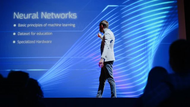 Successful Male Speaker Gets on Stage, Greets Audience and Does Presentation of the Technological Product, Shows Infographics, Statistics Animation on Screen. Live Event / Start-up Conference