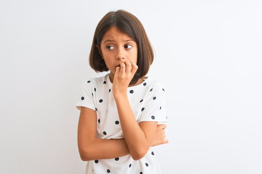 Young beautiful child girl wearing casual t-shirt standing over isolated white background looking stressed and nervous with hands on mouth biting nails. Anxiety problem.