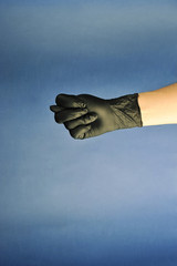 Hands in black latex gloves.  To give someone a finger. The thumb between the pointer and middle fingers form a cookie.  Blue background.  Close-up.  Concept: finger gestures.