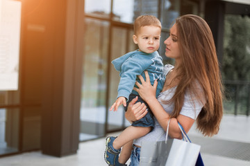 Mother and son walk with packages near mall after shopping .