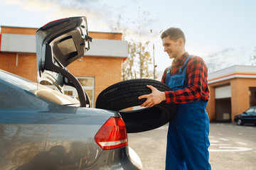 Male worker in uniform puts tyre into the trunk