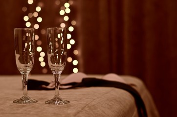 Two glasses with outgoing warm lights sideways on the bed with a discarded bra and tie.