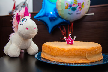 Homemade cake with candle, unicorn plush toy on balloons background