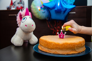 Homemade cake with candle, unicorn plush toy on balloons background