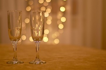 Two transparent wine glasses a soft beige surface with a dim light background of white curtains and lanterns garlands.