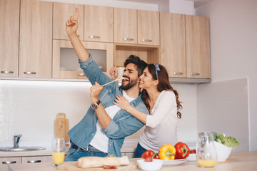 A young couple fooling around - singing, while making a meal.