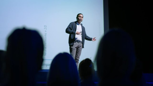 Successful Male Speaker Presents Technological Product, Shows Infographics, Statistics Animation on Big Screen, Talks About Device Performance. Live Event / Device Release / Start-up Conference