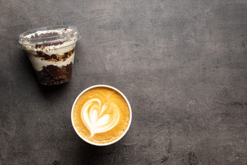 Dessert in plastic container and cup of cappuccino top view on grey background
