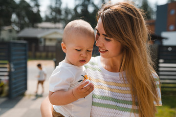 Young mother playing and having fun with her baby boy son brothers in a green garden with cars -...