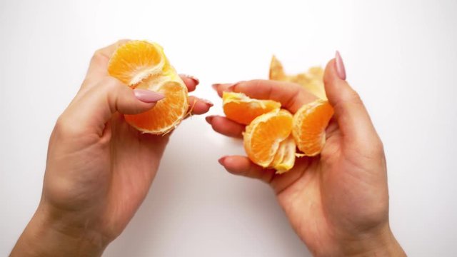 Hands clean tangerine with slices. Peeling process of mandarin on white background