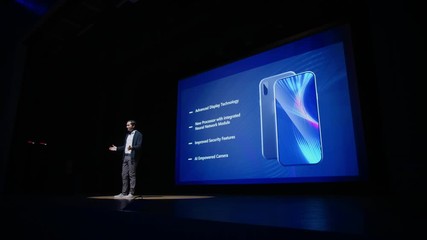 Live Event with Brand New Products Reveal: Speaker Presents Smartphone Device to Audience. Movie Theater Screen Shows Mock-up Touch Screen Mobile Phone with High-Tech Features and Top Highlights