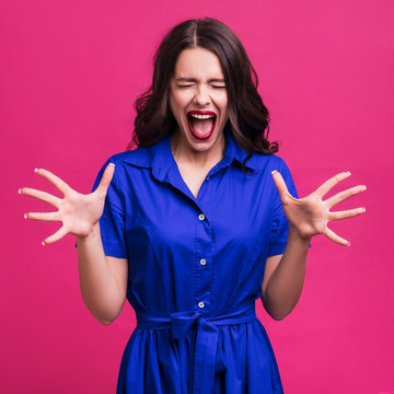 Brunette caucasian woman in blue dress on ponk background. She cries out loud, scared. Emotional portrait with copy space