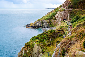 Train exiting a tunnel. View from Cliff Walk Bray to Greystones with beautiful coastline, cliffs and sea, Ireland - obrazy, fototapety, plakaty