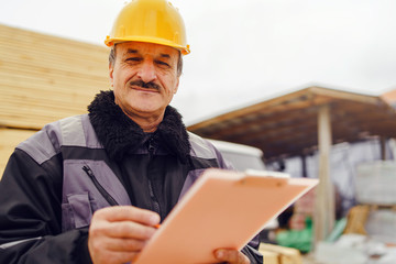 Portrait of caucasian senior man construction worker general laborer building contractor wearing yellow protective helmet holding pen and document checking data report project on the site