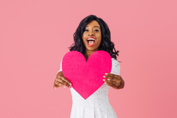 Portrait of an excited young happy woman holding pink heart in front of her with big happy smile, valentineÕs day love,  give your heart concept