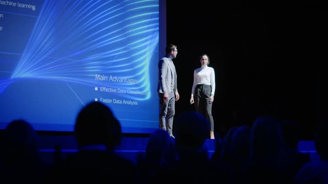 On Stage, Inspirational Female CEO and Male COO Speakers Present Company's New Product, Show Infographics, Statistics on Big Screen, Talk About Growth. Live Event, Tech Startup, Business Conference