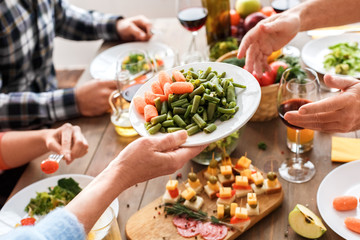 People sitting at home behind table, holding plate with food in hands