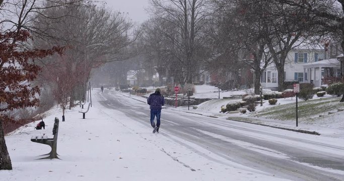 A man walks his dog in a residential neighborhood while snow falls. Pittsburgh suburbs.  	