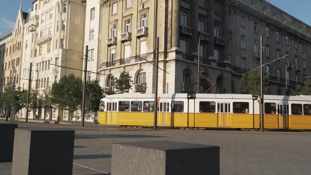 Tram crossing in front of Budapest Parliament, with people walking around. Dolly shot