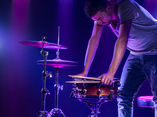 Obraz premium A drummer plays drums on a blue background. Beautiful special effects of light and smoke. The process of playing a musical instrument.