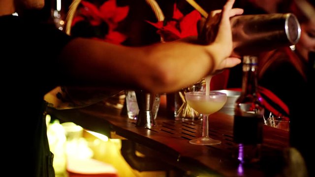 Party at the club. Behind the bar, the bartender prepares cocktails and decorates them with cinnamon. The bartender pours champagne into glasses.