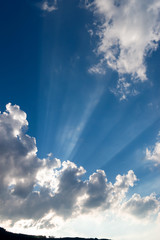 Sunbeam on the blue sky with a dark and white clouds. Sun rays. Sunlight. Divine light and sky. Sunny background.