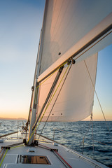 Chasing the sun at sailing yacht. Deck and sails of sailoat pointing to the sunrise. Mediterranean sea, Italy.