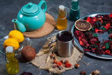 Red Hot Hibiscus tea in a glass mug on a wooden table among rose petals and dry tea custard with carcade