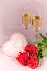 Valentine's day card, two glasses of champagne on a pink background red roses and a pink heart, a lit candle