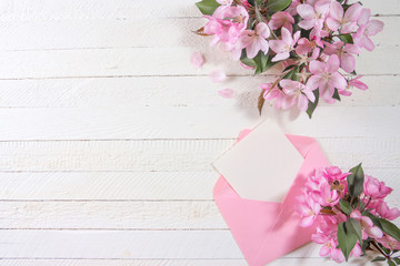 Card with pink envelope and pink flowers on wooden board.
