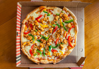 Freshly opened pizza with cheese and tomato dough, chicken, red, yellow and green peppers in a folded box. Noisy shot on purpose