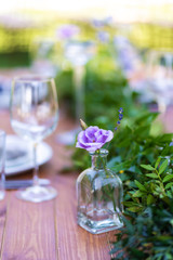 A wooden table without a tablecloth is served and decorated with fresh flowers. Details of festive decorations with fresh flowers