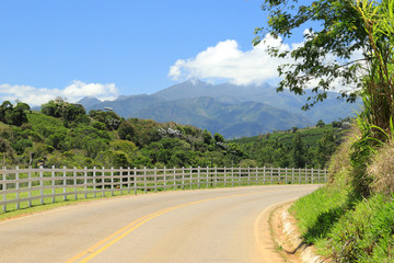 A country roads leading to the Caparaó National Park (mountain ranges in the background), where is...