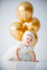 Fototapeta na wymiar A one year old, baby girl sitting with a bunch of golden balloons on white background in studio