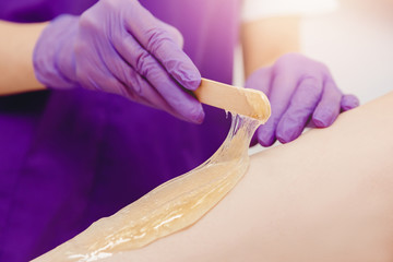 Application of sugar paste for shugaring depilation with scraper on skin of girl legs. Hair removal...