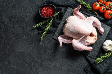 Raw whole poult with rosemary and pink pepper. Black background. Top view. Space for text
