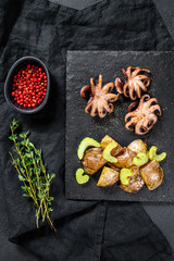 Roasted octopus. Baked potatoes and celery. Black background. Top view